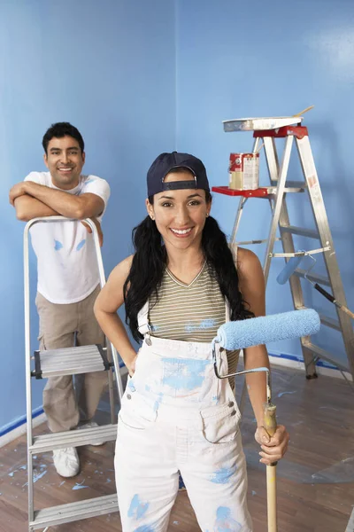 Portrait of happy couple painting blue color on wall