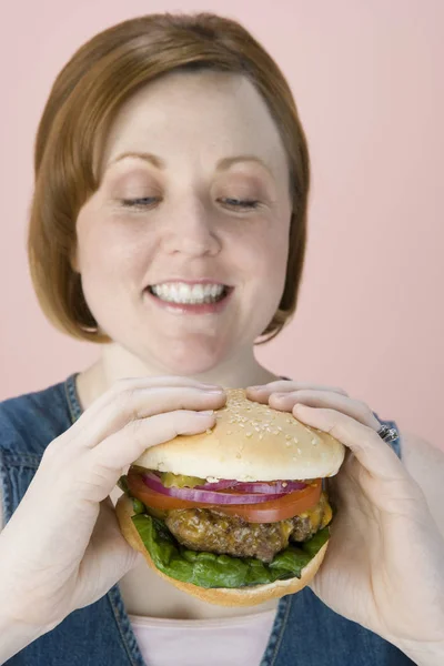 Mujer Hermosa Feliz Mirando Hamburguesa Sobre Fondo Rosa — Foto de Stock