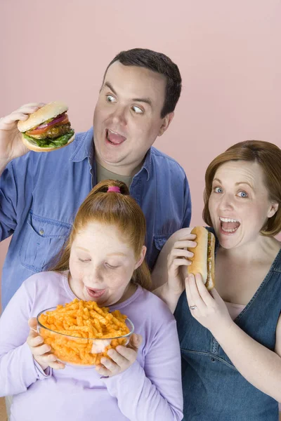 ピンクの背景に隔離されたジャンクフードを食べる肥満家族 — ストック写真