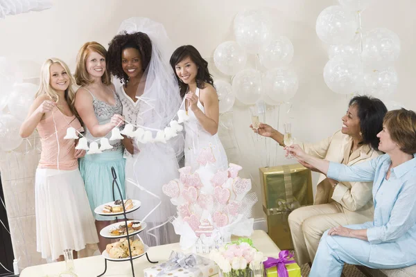 Portrait of bride and her friends holding wedding bells with women toasting champagne at hen party