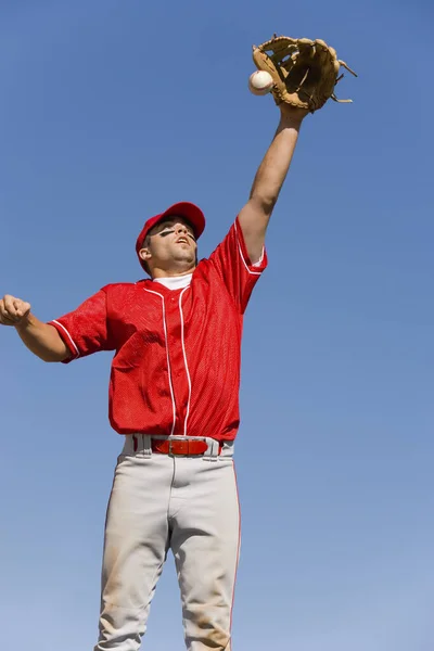 Baseball player trying to catch ball against clear sky
