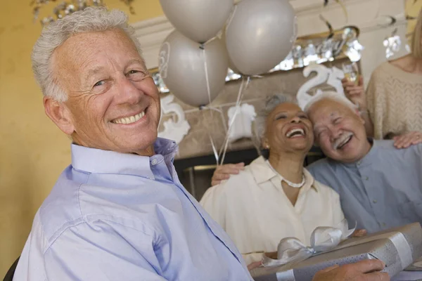 一个快乐的老人和朋友在背后笑着拿着礼物的画像 — 图库照片