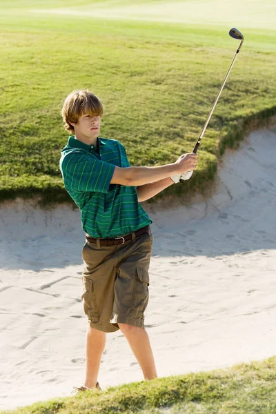 Young man hitting golf ball out of a sand trap