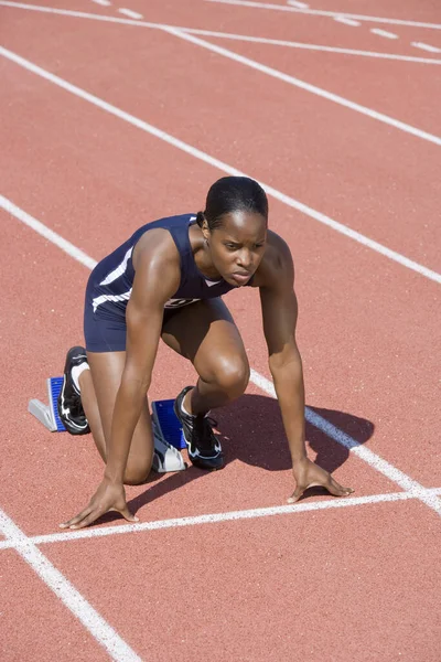 Full length of African American female athlete at starting line on running track