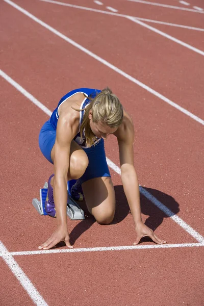 Full length of Caucasian female athlete ready to race on track and field