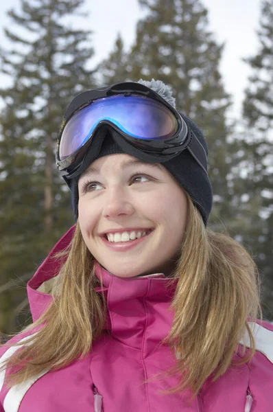 让快乐的年轻女子穿着粉红雪衣 戴着滑雪眼镜 背对着树木 — 图库照片