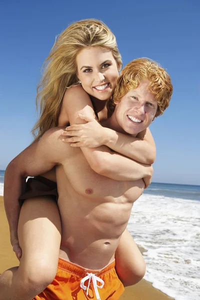 Portrait of a happy young man piggybacking woman on beach