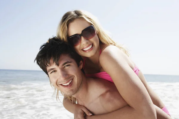 Portrait of happy man piggybacking woman on beach
