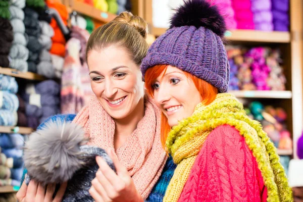 Young women buying colorful bobble hat in knitting fashion textile store