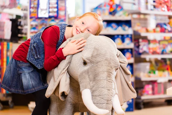 Little girl in toy store cuddling with stuffed animal, shelves with toys in the background