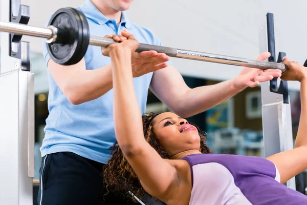 Black woman with Trainer lifting weights on barbell in gym for fitness