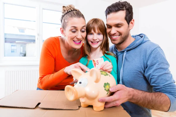 Family saving money by moving house putting bank note in piggybank