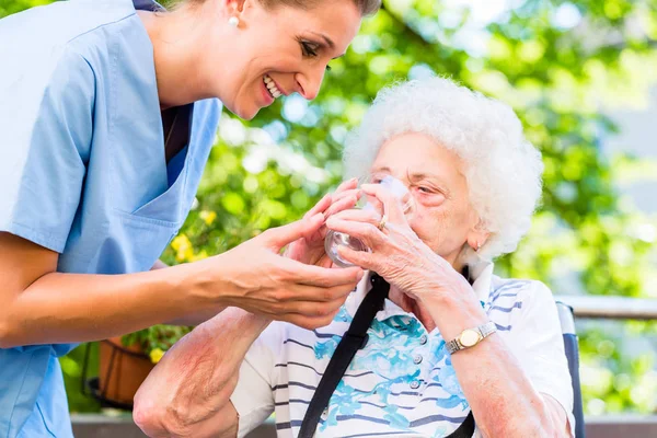 年配の看護師が年配の女性にコップ一杯の水を与える — ストック写真