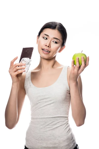 滑稽的年轻女人 一边看着巧克力吃一个新鲜的苹果 — 图库照片