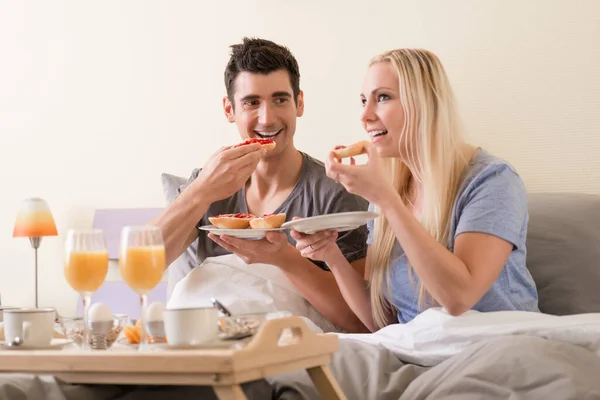 ベリージャムを食べながらベッドで朝食を祝う若いカップルOトースト新鮮なオレンジジュースとゆで卵を伴う — ストック写真
