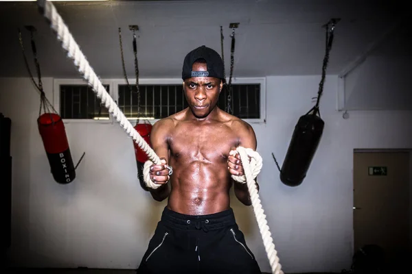 Portrait of young determined man waving battle ropes during high-intensity training indoors