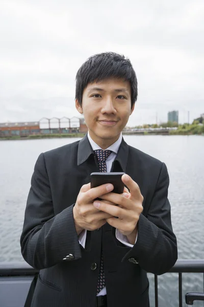 Portrait of confident businessman text messaging through cell phone outdoors