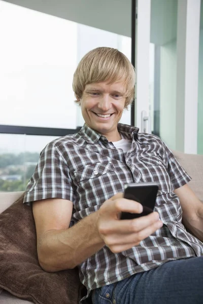 Lächelnder Mittlerer Erwachsener Mann Sms Auf Dem Heimischen Sofa — Stockfoto