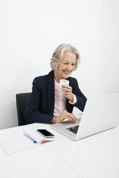 Sonriente Mujer Negocios Senior Tomando Café Mientras Usa Computadora Portátil — Foto de Stock