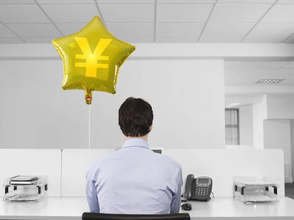 Rear view of mid-adult man working with Yen sign on balloon in office