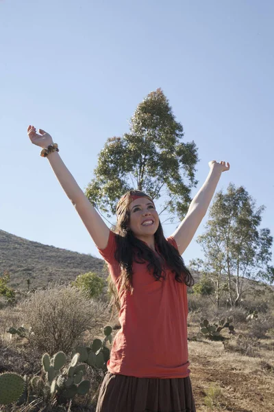 Hispanic woman with arms raised standing outdoors
