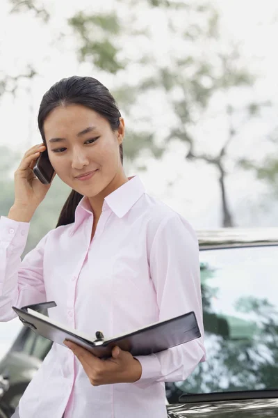 Chinese businesswoman holding notebook and talking on cell phone