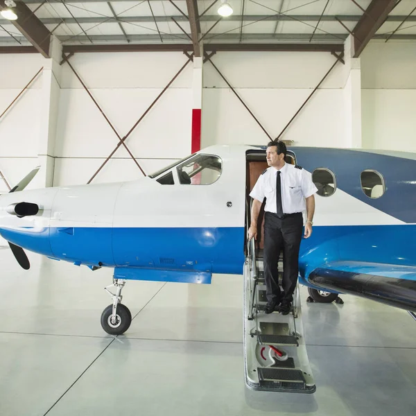 Caucasian pilot disembarking airplane in hangar