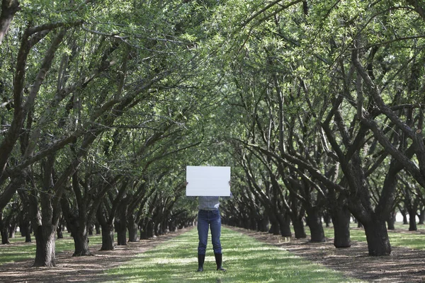 Caucasian woman holding blank placard underneath trees