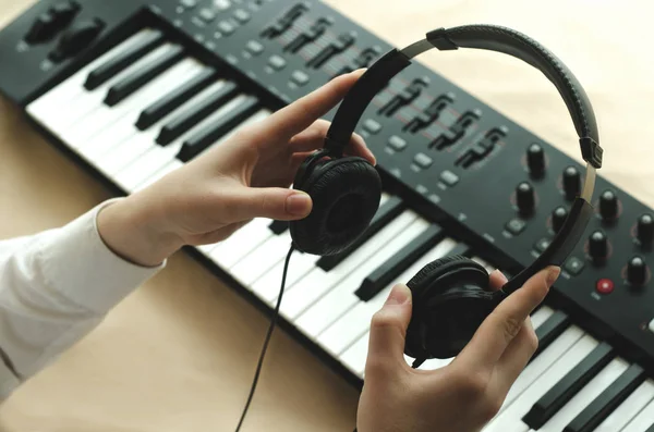 stock image Woman in white shirt holds the headphones on the background of the synth. In the frame two hands.