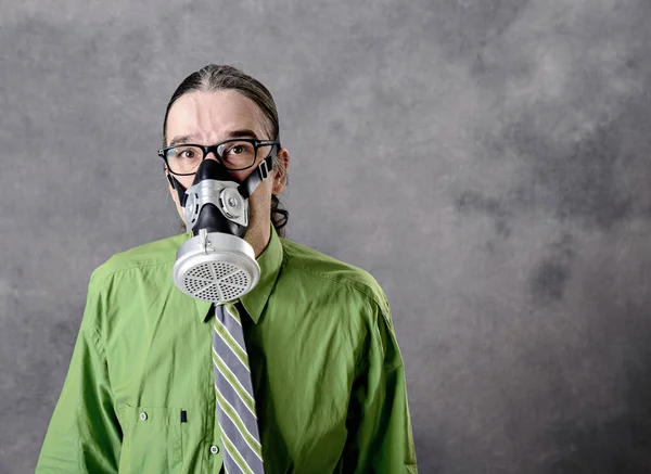 灰色の背景の前にガスマスクをした緑色のシャツを着た若いビジネスマン — ストック写真