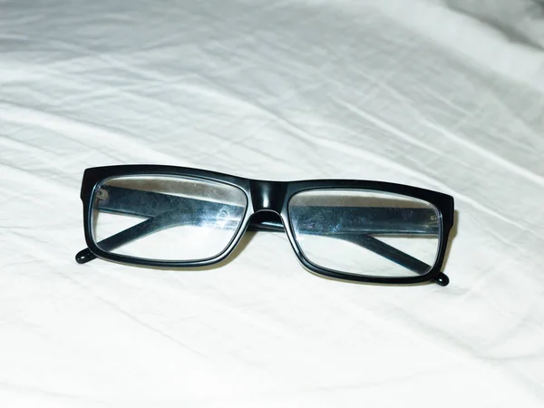 把黑色的眼镜叠起来 放在白色的床单上 — 图库照片
