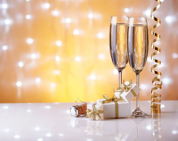 Two glasses with champange, gift boxes and christmas decorations on a yellow background with lights of garland.  New year and Christmas.