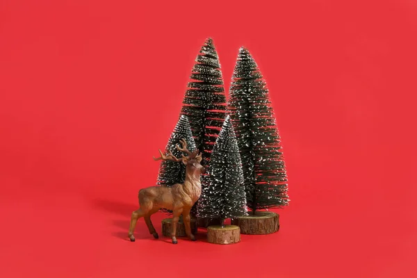 孤立的一群完整的人工冷杉 像一棵小森林树 里面有一只小驯鹿 背景是鲜艳的红色 最小静生活摄影 — 图库照片