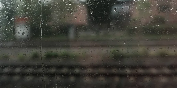 窓には雨が降り背景にはぼやけたレールがあり — ストック写真