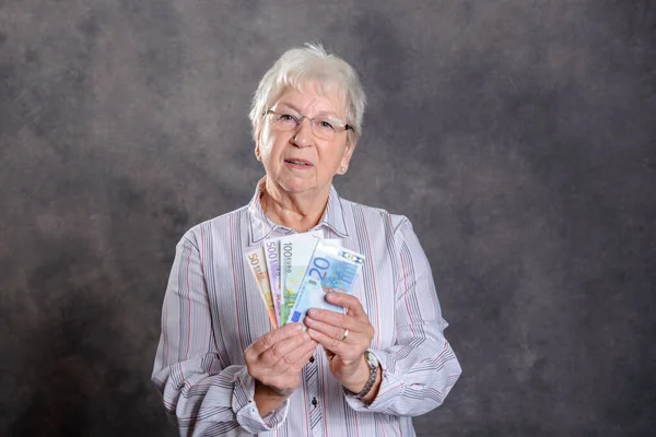 happy gray hairy elderly woman with money in front of gray background