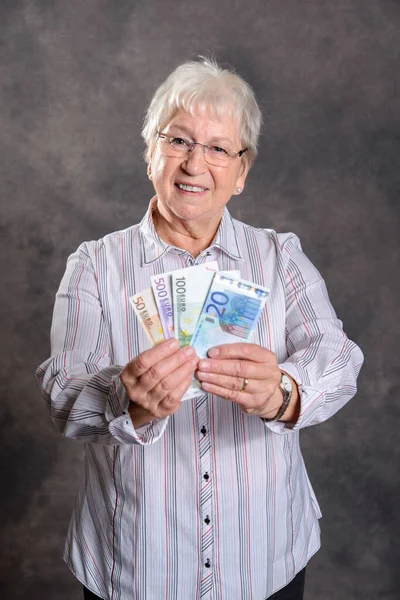 happy gray hairy elderly woman with money in front of gray background