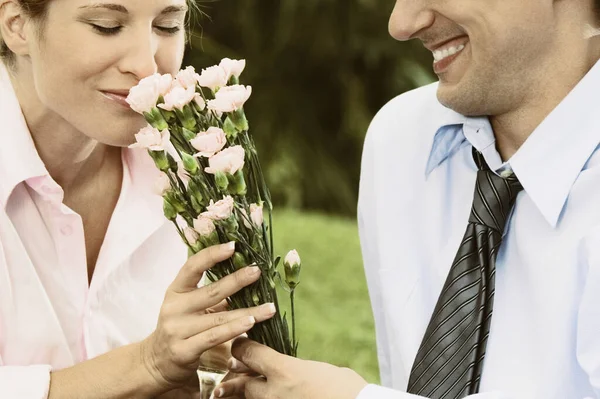 Mid section view of a mid adult man giving flowers to a young woman