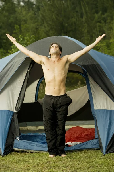 Mid adult man standing in front of a dome tent with his arms outstretched