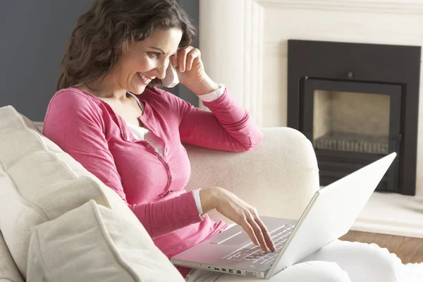 Evde Kanepede Oturan Dizüstü Bilgisayar Rahatlatıcı Kullanan Kadın Telefonda Konuşurken — Stok fotoğraf