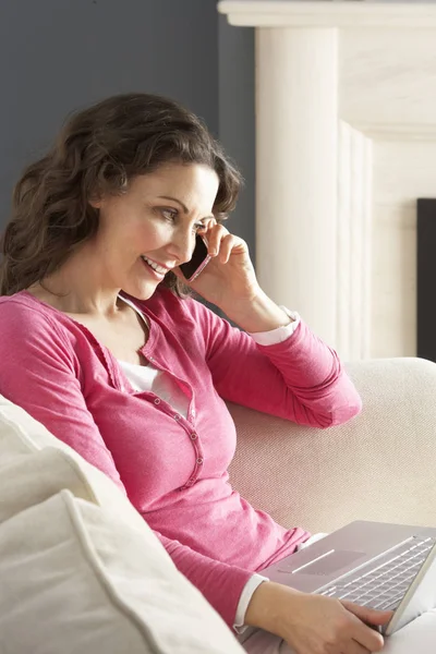 Evde Kanepede Oturan Dizüstü Bilgisayar Rahatlatıcı Kullanan Kadın Telefonda Konuşurken — Stok fotoğraf