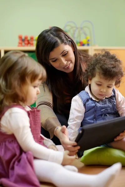 白人女性教育者と小さな女の子読書おとぎ話オンタッチパッドコンピュータで幼稚園 — ストック写真