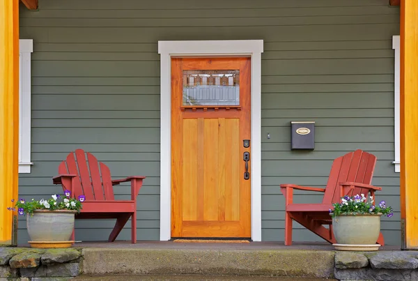 Mission style Stained wood front door with beveled glass surrounded by two Adirondack chairs and flowers