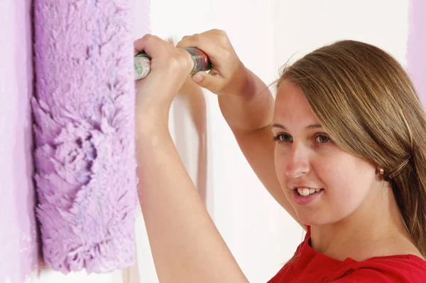 穿着五颜六色衬衫的年轻女子用彩绘滚筒触摸着她的第一个公寓 — 图库照片
