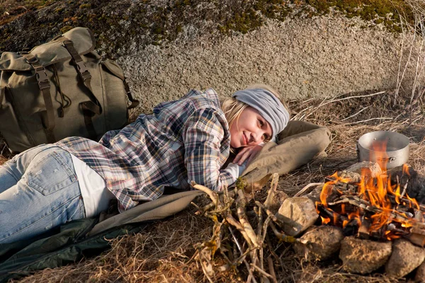 Young hiking woman with backpack sleep by campfire countryside