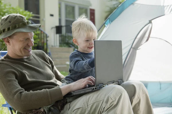 Father and son on laptop computer camping in the front yard