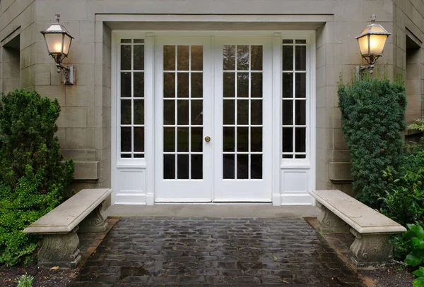 Elegant stone walkway bordered by stone benches leading to a double glass paned front door with two large front lanterns