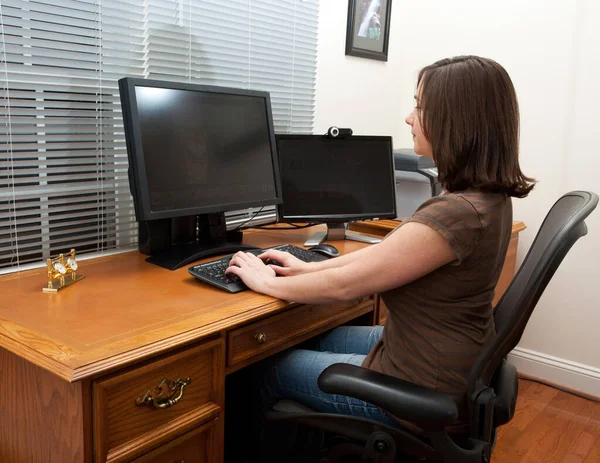 革の机の上に2つのモニターとキーボードを持つホームオフィスの若い女性とキーボードの入力 — ストック写真