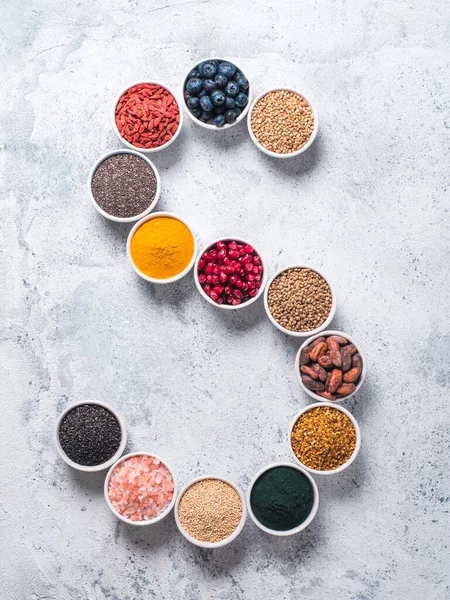Above view of various superfoods in smal bowl in form S letter on gray background. Superfood as chia,spirulina,cocoa bean,goji,hemp,blueberry,quinoa,bee pollen,black sesame,turmeric. Top view,flat-lay