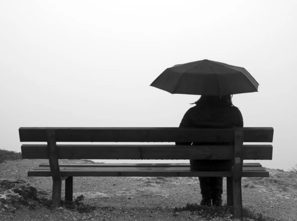 崖の端のベンチに座っている傘を持つ女性 — ストック写真