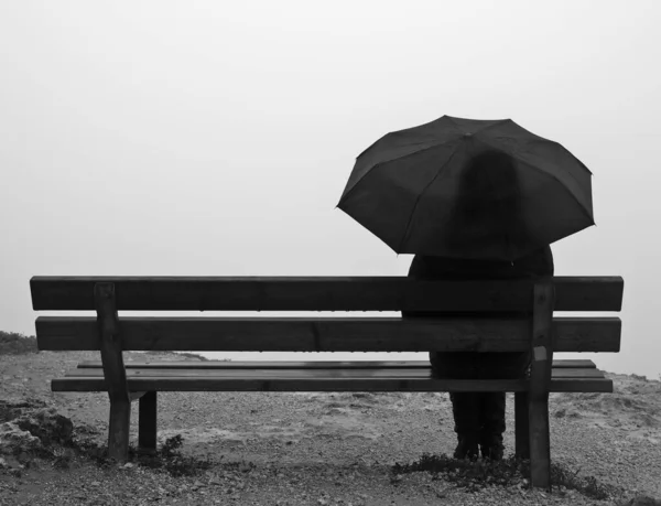 一个带伞的女人坐在悬崖边的长凳上 — 图库照片